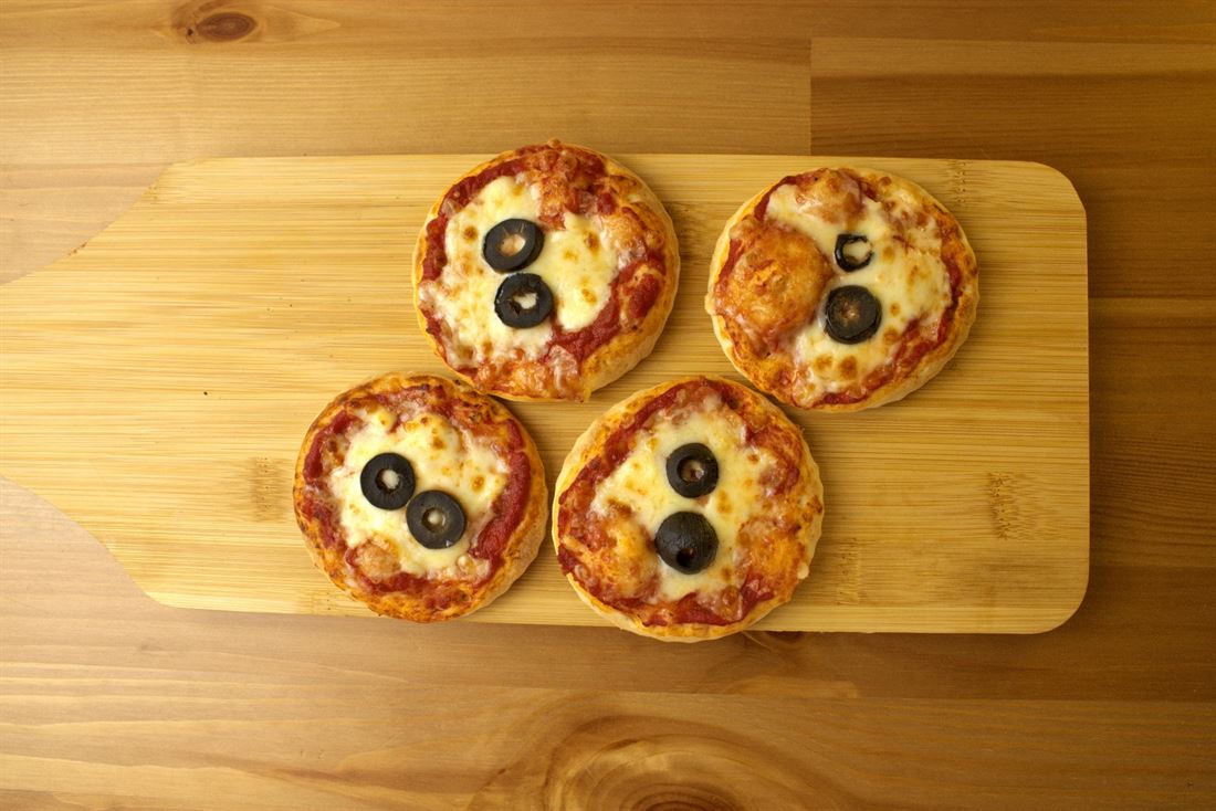Four mini pizza pies with olives on a wooden board